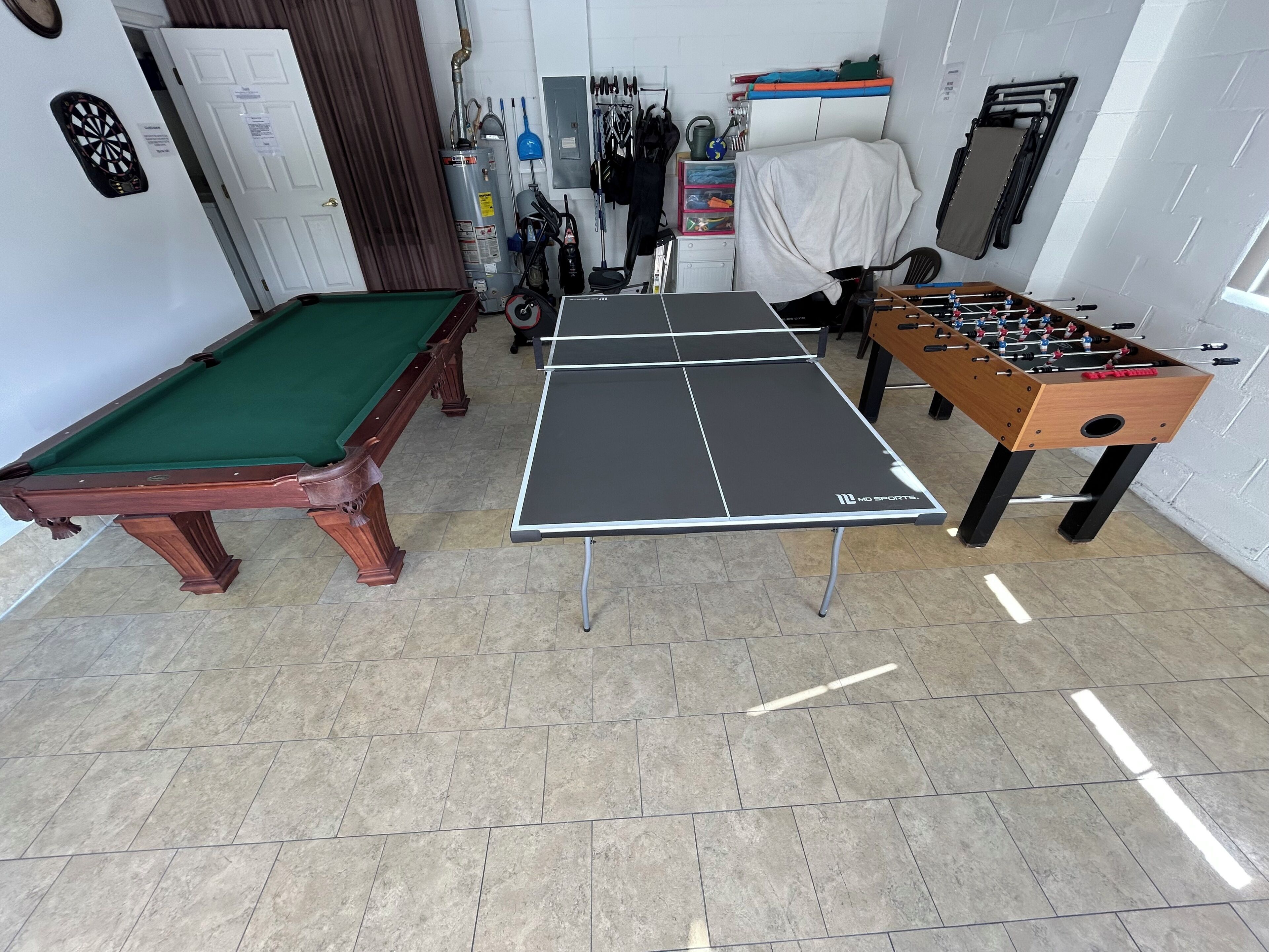 A billiards table, a foosball table, and a pool table in a room with tiled flooring and various sports equipment.