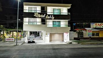 Un hôtel de deux étages, avec une enseigne indiquant « Hôtel Ashly » et une entrée bien visible, devant laquelle est garée une voiture.