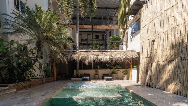 A swimming pool with a thatched roof structure, surrounded by potted plants and lounge chairs. - Hotel Ashly (Acapulco)