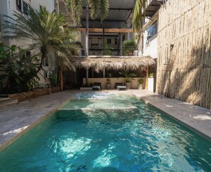 A swimming pool with a thatched roof structure, surrounded by potted plants and lounge chairs. - Hotel Ashly (Acapulco)