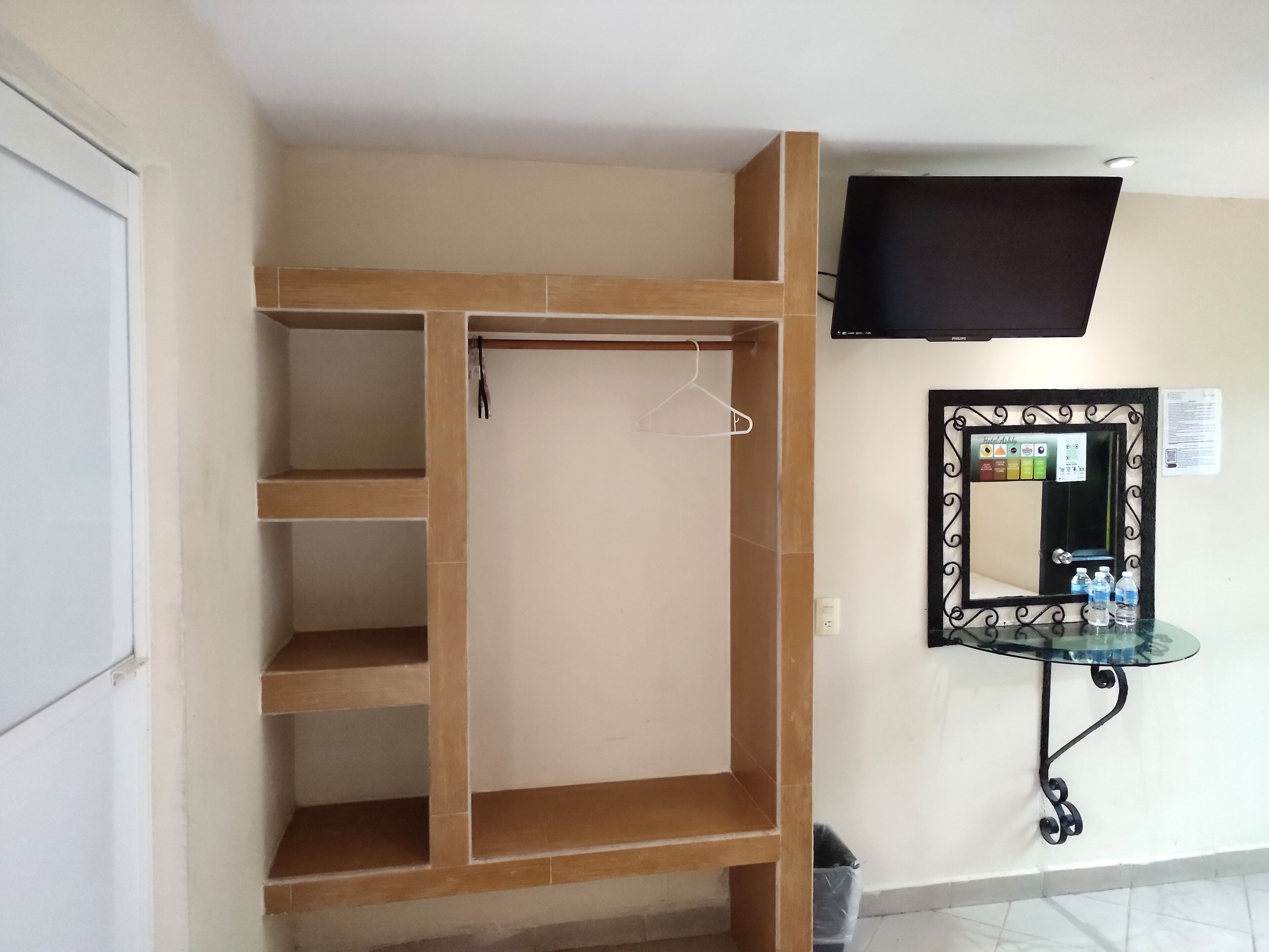 A room with a wooden wardrobe, a mirror with a decorative frame, and a mounted television.