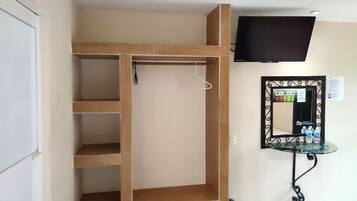 A room with a wooden wardrobe, a mirror with a decorative frame, and a mounted television.