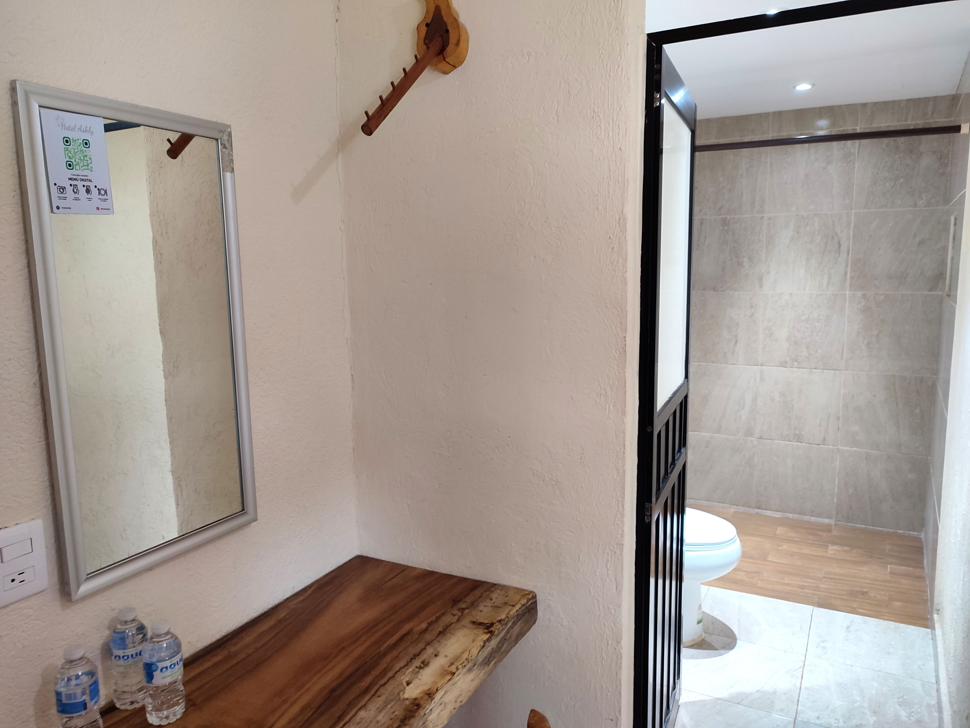 Une salle de bain avec un meuble-lavabo en bois, un miroir et une clé accrochée au mur. On peut voir des bouteilles d’eau sur le meuble-lavabo.