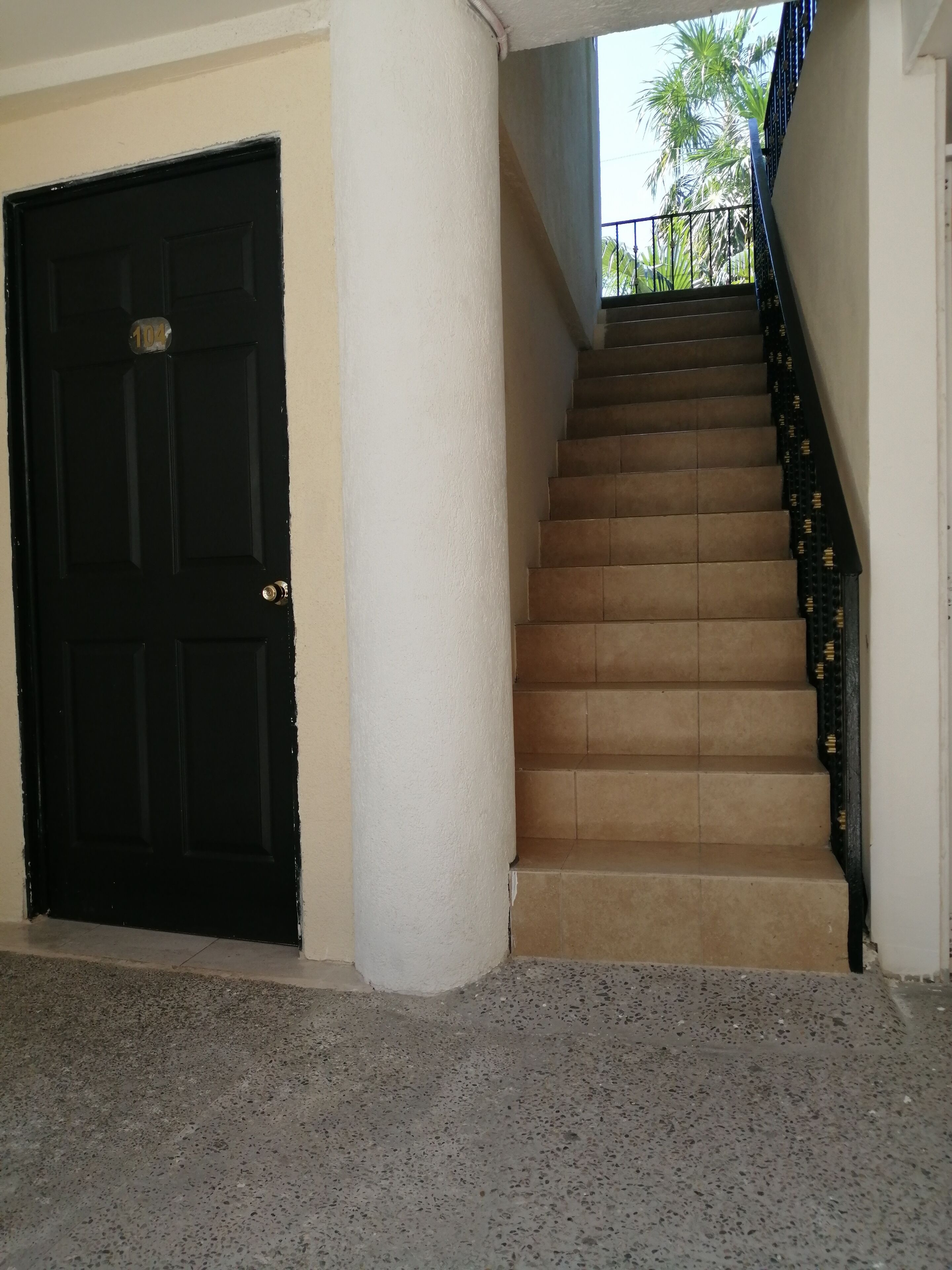 A staircase with beige steps leading to a balcony, a black door with a number plate, and a white wall.