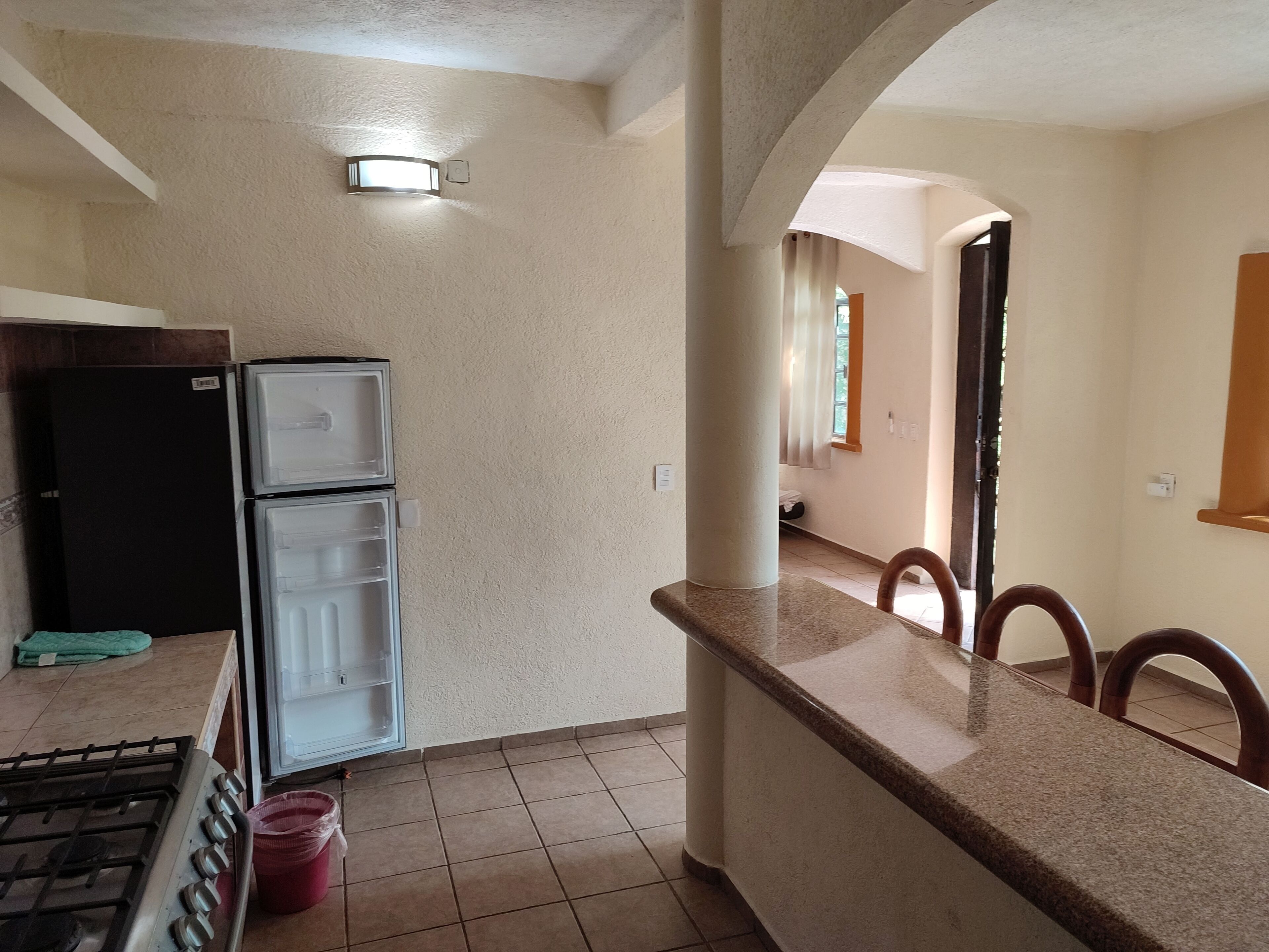 A kitchen with a gas stove, a black refrigerator, and a double-door refrigerator.