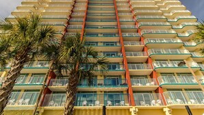 A multi-story hotel with balconies, palm trees, and a clear sky.