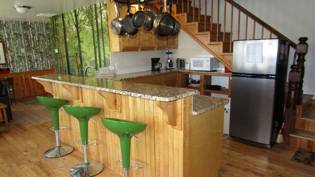 Una cocina con taburetes de madera, un refrigerador de acero inoxidable y una escalera de madera.