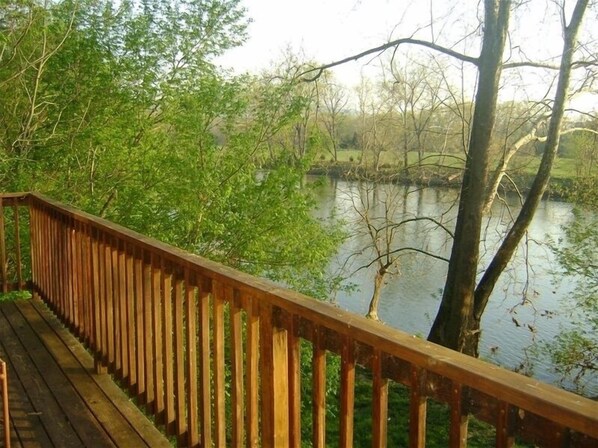 A wooden deck overlooking a calm lake with dense greenery and trees in the background.
