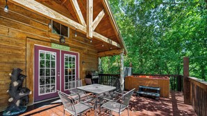 A cabin with a patio featuring metal chairs and a table, a grill, and a hot tub.