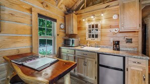 A wooden cabin kitchen with a wooden table, a microwave, a sink, and a refrigerator.