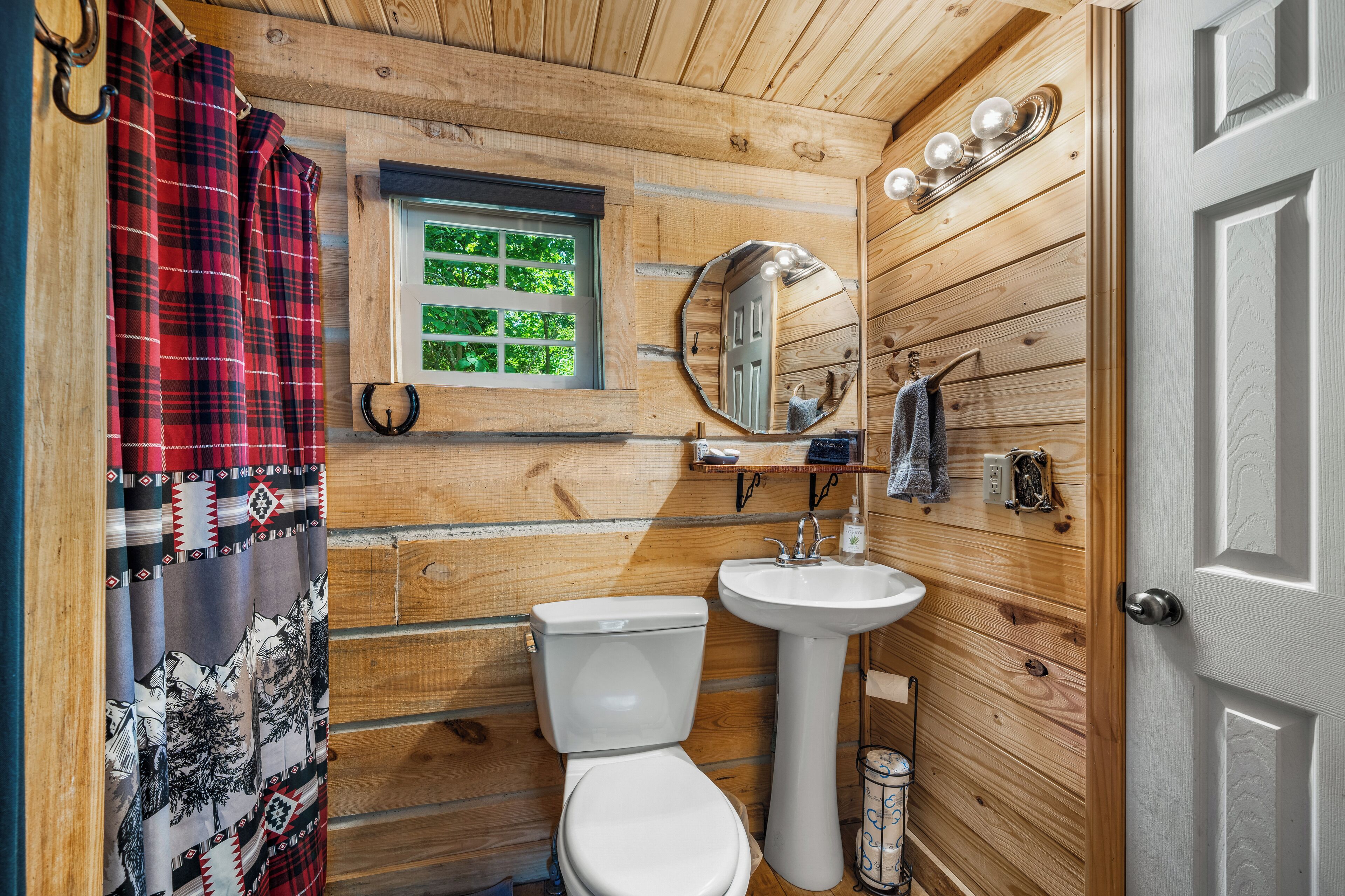 A wooden cabin bathroom with a white toilet, sink, and a mirror above the sink.