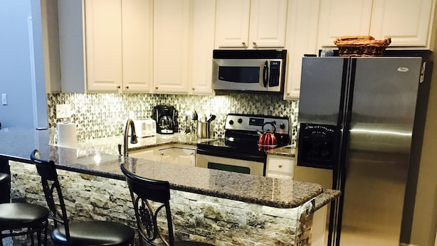 A kitchen with a granite countertop, stainless steel appliances, and black bar stools.