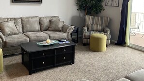 A living room with a grey sofa, a black coffee table, a patterned armchair, and a large plant.