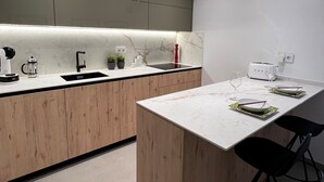 A modern kitchen with wooden cabinets, a marble countertop, and a dining area with a white table and black chairs.