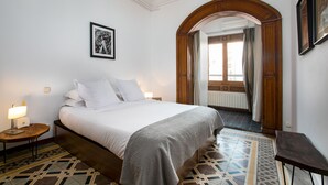A hotel room with a large bed, a nightstand, a lamp, a framed picture on the wall, and a patterned floor.