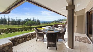 A covered patio with a table and chairs, a stone wall, and a view of a green landscape and trees. - The Most Gorgeous OV Villa in Kapalua Sleeps 6 (Kapalua)
