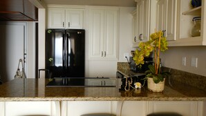 A kitchen with white cabinets, a black refrigerator, granite countertops, and a bar area with stools. - Stay On The Beach In Makaha   (Waianae)