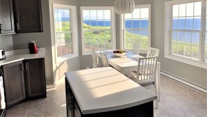 A kitchen with a view of the ocean, a dining table with chairs, and a hanging light fixture.