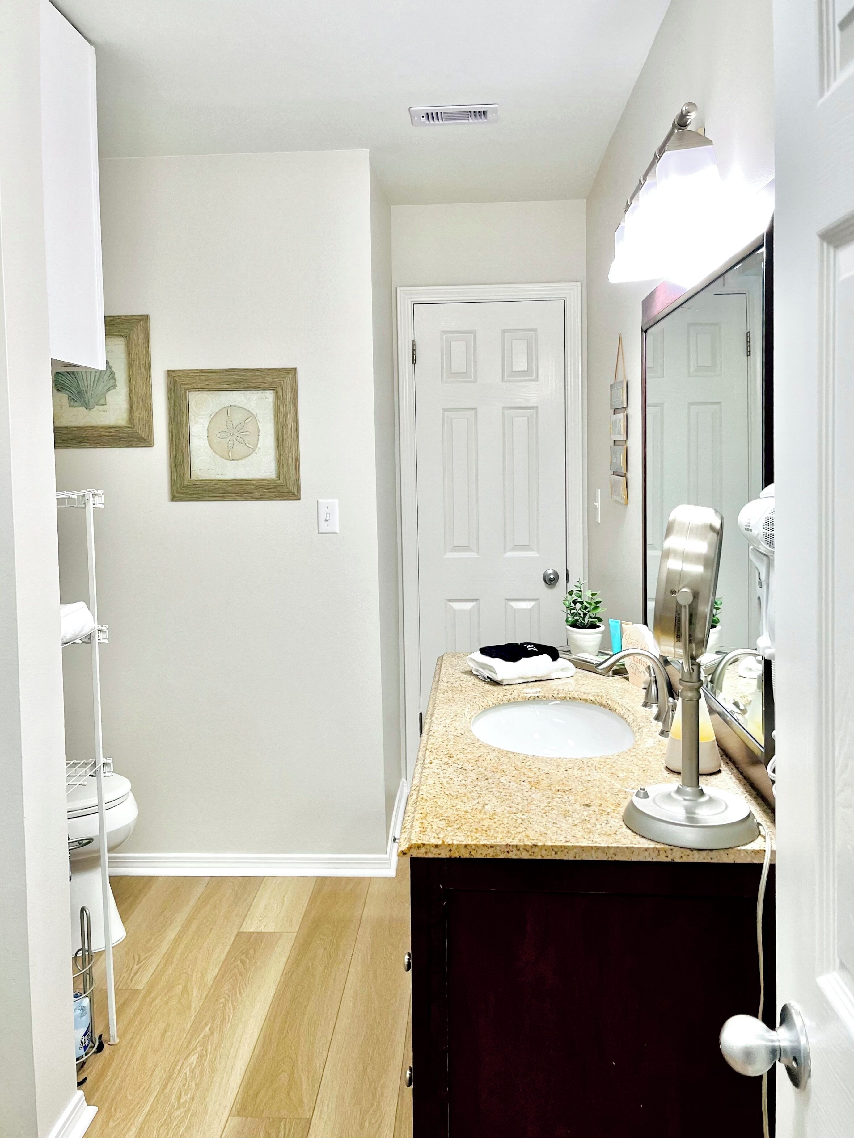 A bathroom with a sink, mirror, vanity, and a door leading to another room.