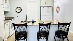 A kitchen with white cabinets, a microwave, a stove, a sink, a clock, a refrigerator, and three bar stools. - Private Beach & Free Beach Service; Walkable Scenic 98 to Dining; Pool & Hot Tub (Miramar Beach)