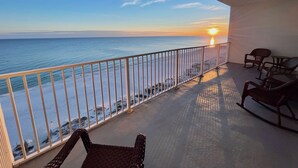 Een balkon met uitzicht op de oceaan bij zonsondergang, met een hekwerk, een schommelstoel en een tafel.