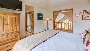Ein Schlafzimmer mit einem großen Bett, einem Holzschrank, einem Flachbildfernseher, einem Spiegel und Blick auf einen Balkon.