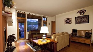 A cozy living room with a sofa, a lamp, and a statue. There are wooden floors and a view of mountains through the window. - Granita 301 (Telluride)
