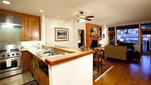 A modern kitchen with wooden cabinets, a central island, and a dining area with a sofa and table. - Granita 301 (Telluride)