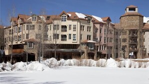 Um hotel com várias andares, fachada de pedra e diversas varandas, rodeado de neve.