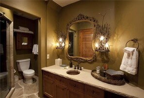Un baño con un espejo grande y ornamentado, dos apliques de pared, un lavabo y un inodoro.