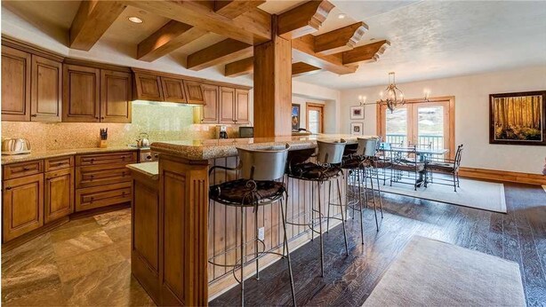 A spacious kitchen with wooden cabinets, a central island with stools, and a dining area with a large table and chairs. - Plaza 403 (Telluride)