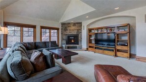 A living room with a stone fireplace, a large TV, and a wooden entertainment center. - Plaza 403 (Telluride)