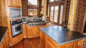 A log cabin kitchen with wooden cabinets, a stainless steel stove, and a granite countertop. - Sundance Grand Overlook (Telluride)