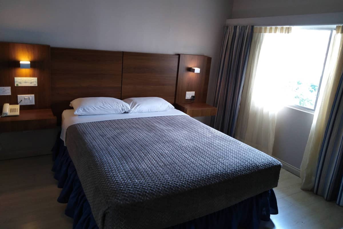 Une chambre d’hôtel avec un grand lit, une tête de lit en bois, des tables de chevet avec des lampes, un téléphone et une fenêtre avec des rideaux.