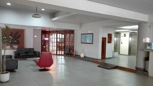 Eine geräumige Lobby mit einem roten Sessel, einer Couch und einem Blumentopf.