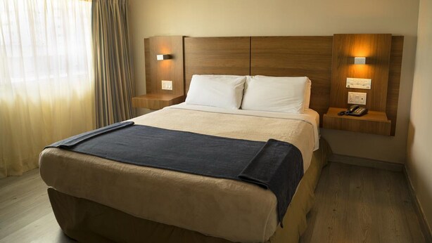 Ein Hotelzimmer mit einem großen Bett, einem Holzkopfende, Nachttischlampen und einem Telefon auf einem Nachttisch.