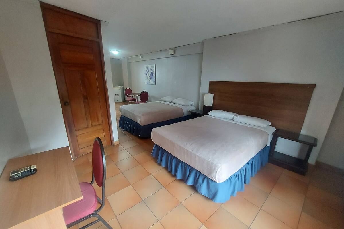 Une chambre d’hôtel avec deux lits, un bureau, une chaise et une petite table avec une lampe.