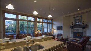 A spacious living area with a fireplace, large windows, and a kitchen with a sink and counter. - Belvedere Park 1 (Telluride)