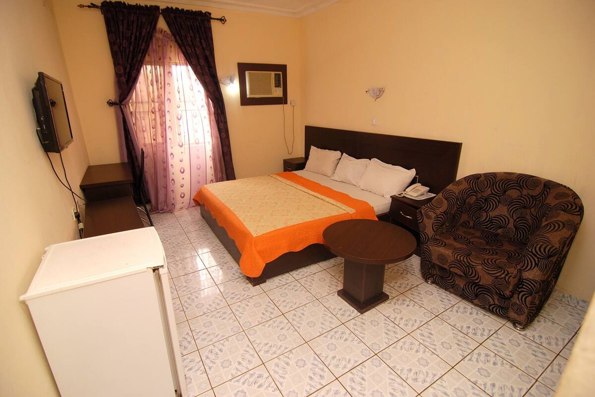 A bedroom with a bed, bedside table, chair, and a small table.