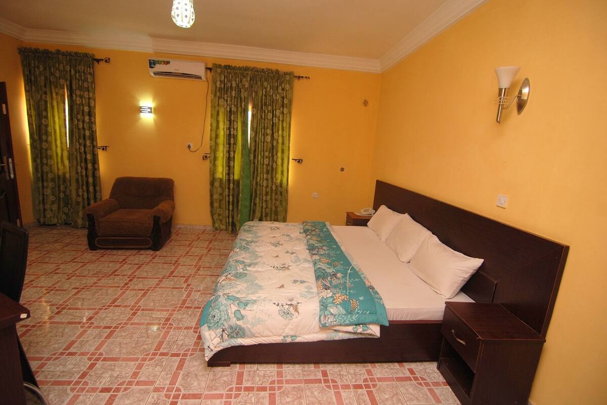 A hotel room with a bed, a chair, a nightstand, and curtains.