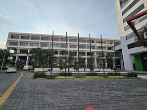 A multi-story building with a modern architectural design, featuring a ground-level commercial area with visible storefronts and a paved walkway in front. - Kharma Suites (San Andrés Cholula)