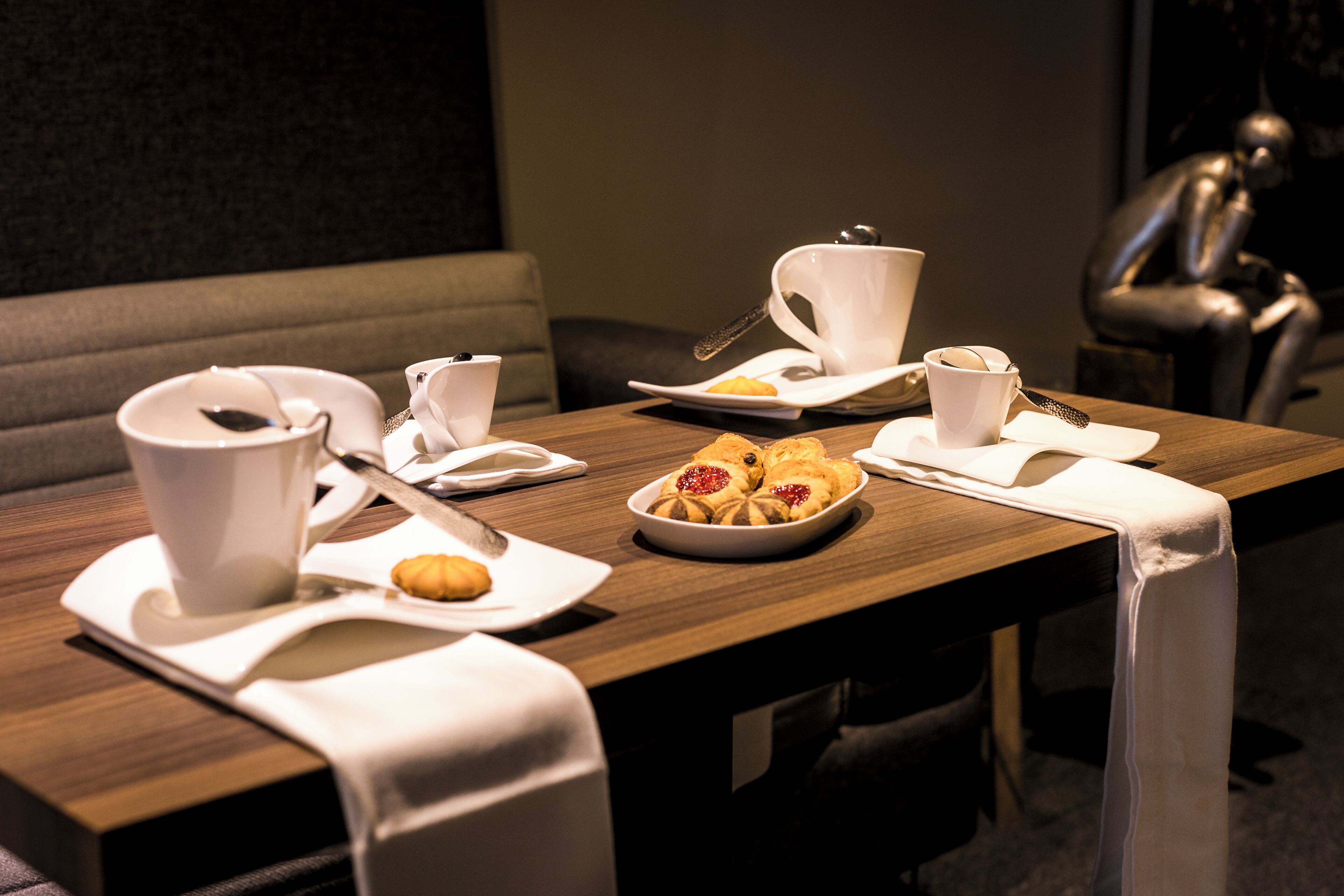 A dining table set with white tableware, including plates, cups, and cutlery, and a bowl of pastries.