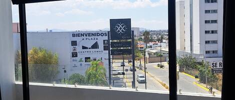 Una habitación de hotel con una cama, un ventanal con vistas a un paisaje urbano y un cartel que dice 'BIENVENIDOS Plaza'.