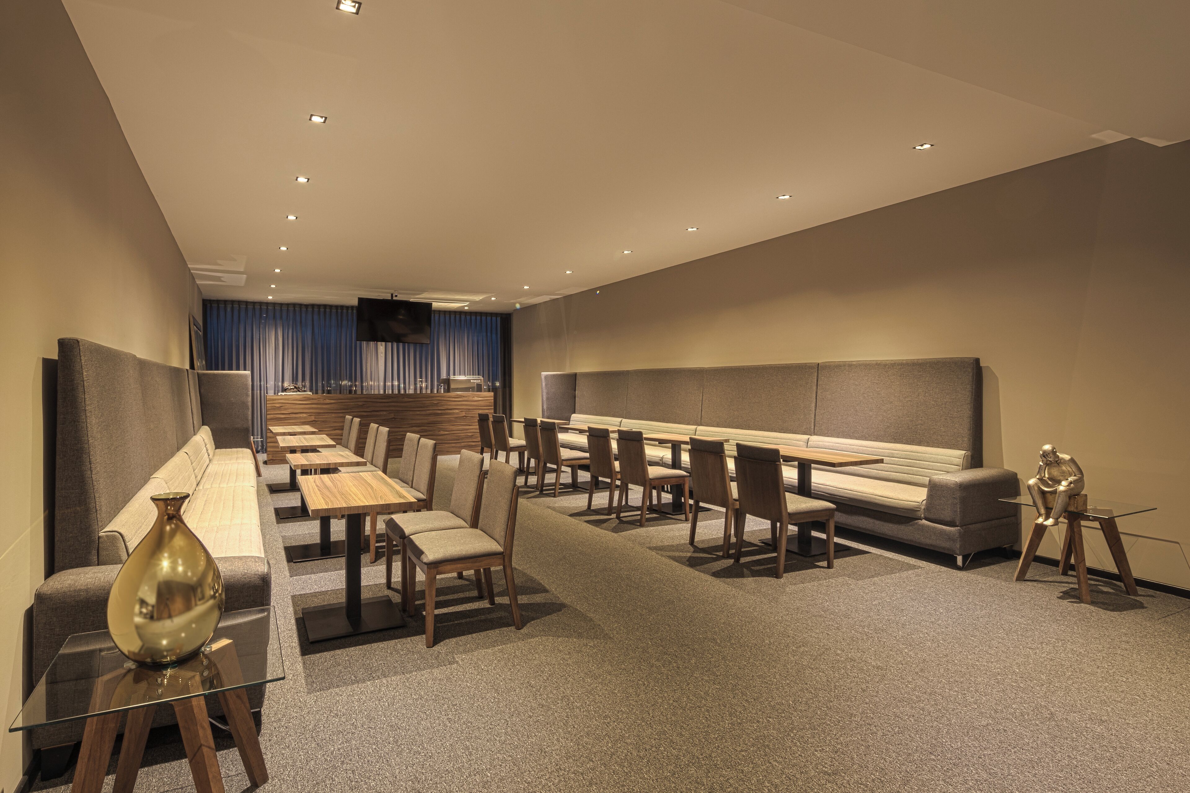 Een moderne hotel lobby met een lange receptiebalie, een zithoek en een aan de muur bevestigde televisie.