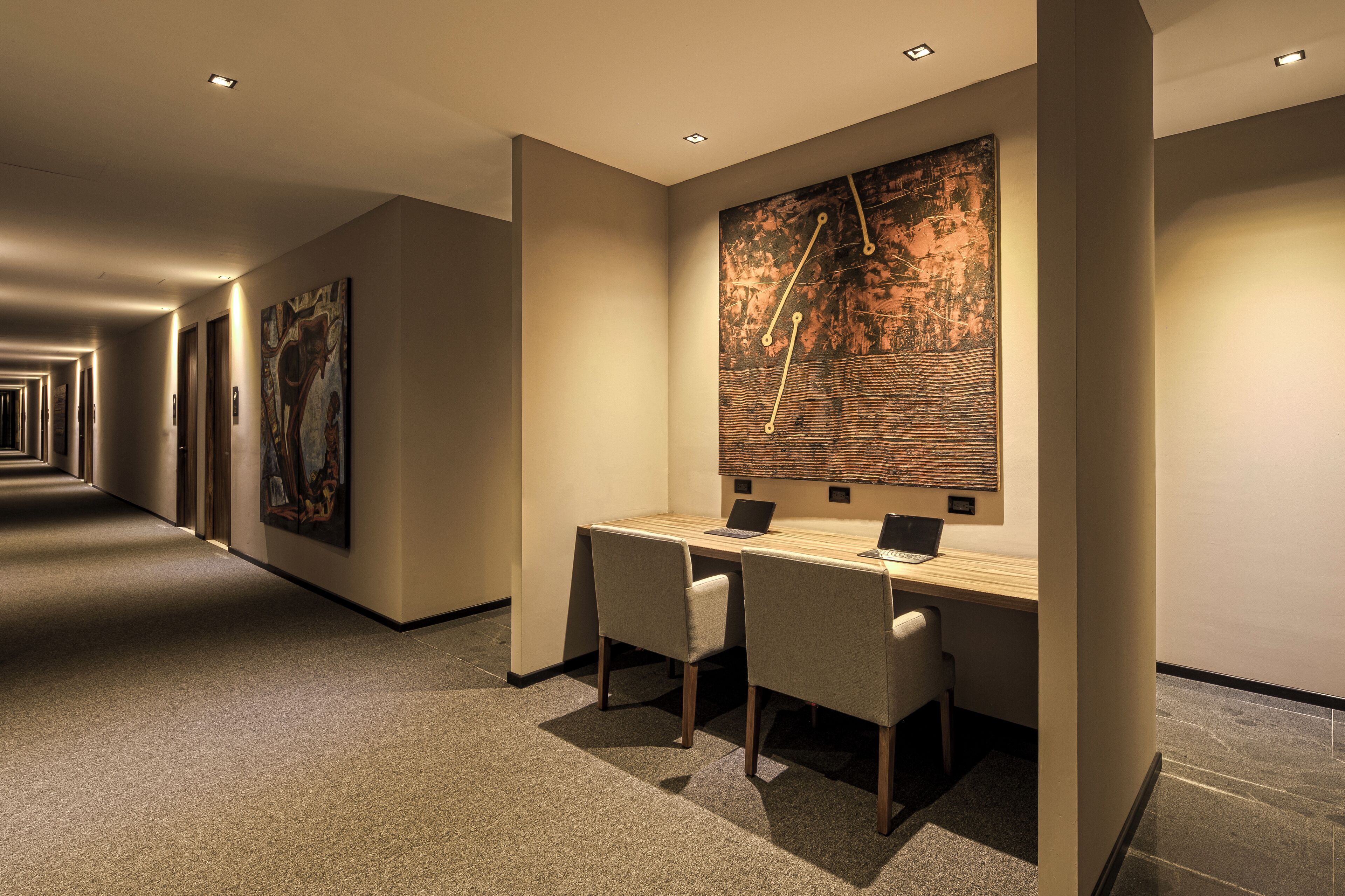 A modern hotel lobby with a long corridor, a reception desk, and artwork on the walls.