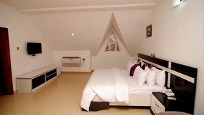 A bedroom with a bed, bedside table, and a TV mounted on the wall. - The Grosvenor Suite (Abuja)
