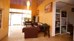 A spacious lobby with a high ceiling, a chandelier, a brown leather sofa, a potted plant, and a staircase leading to an upper floor. - The Grosvenor Suite (Abuja)