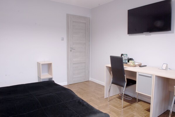 A bedroom with a bed, a desk, a chair, a TV, and a door.