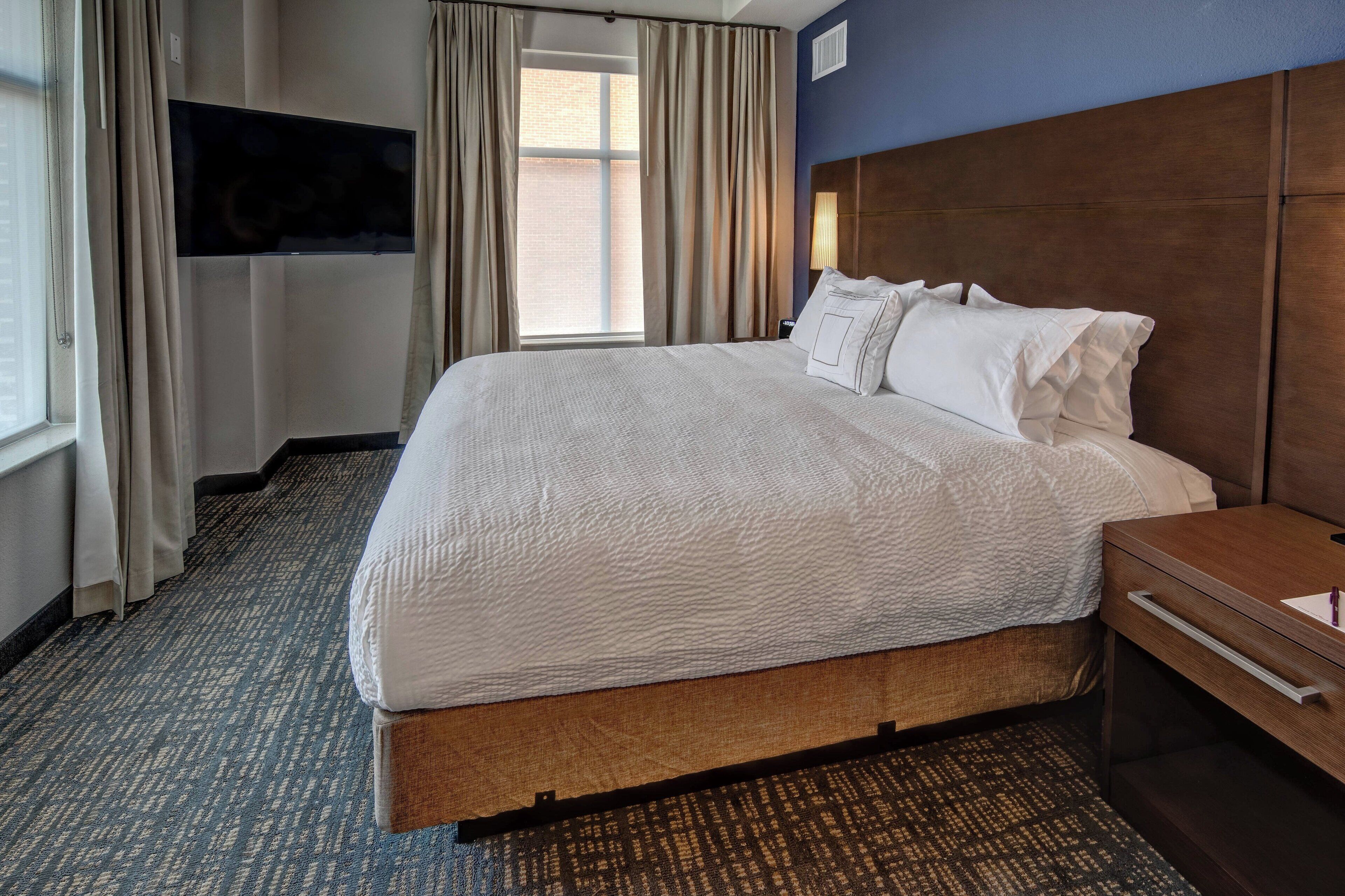 Habitación de hotel con una cama grande, cabecera de madera, televisor de pantalla plana en la pared y una ventana con cortinas.