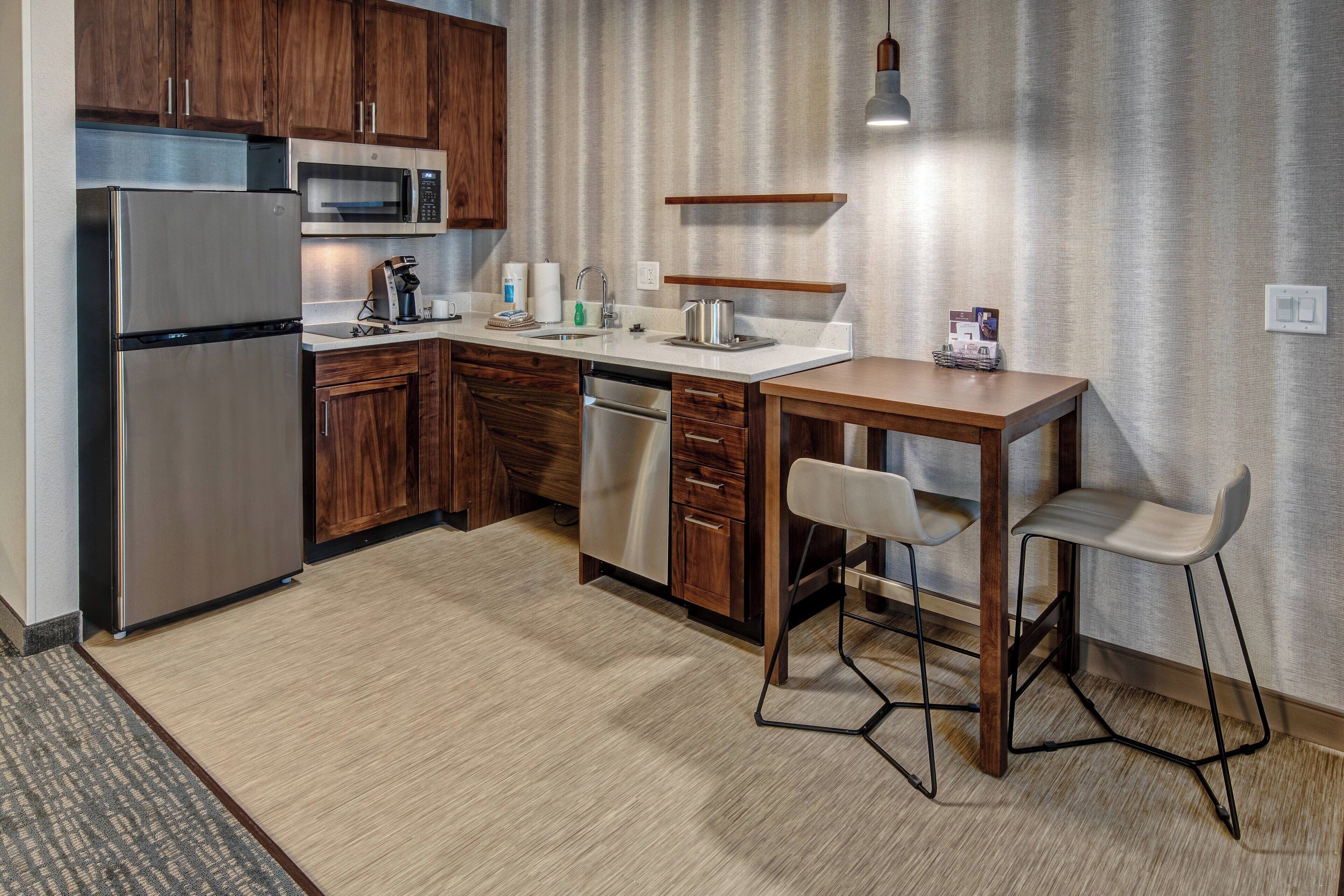 A modern kitchen with wooden cabinets, stainless steel appliances, a built-in microwave, a coffee maker, and a small dining area with stools.